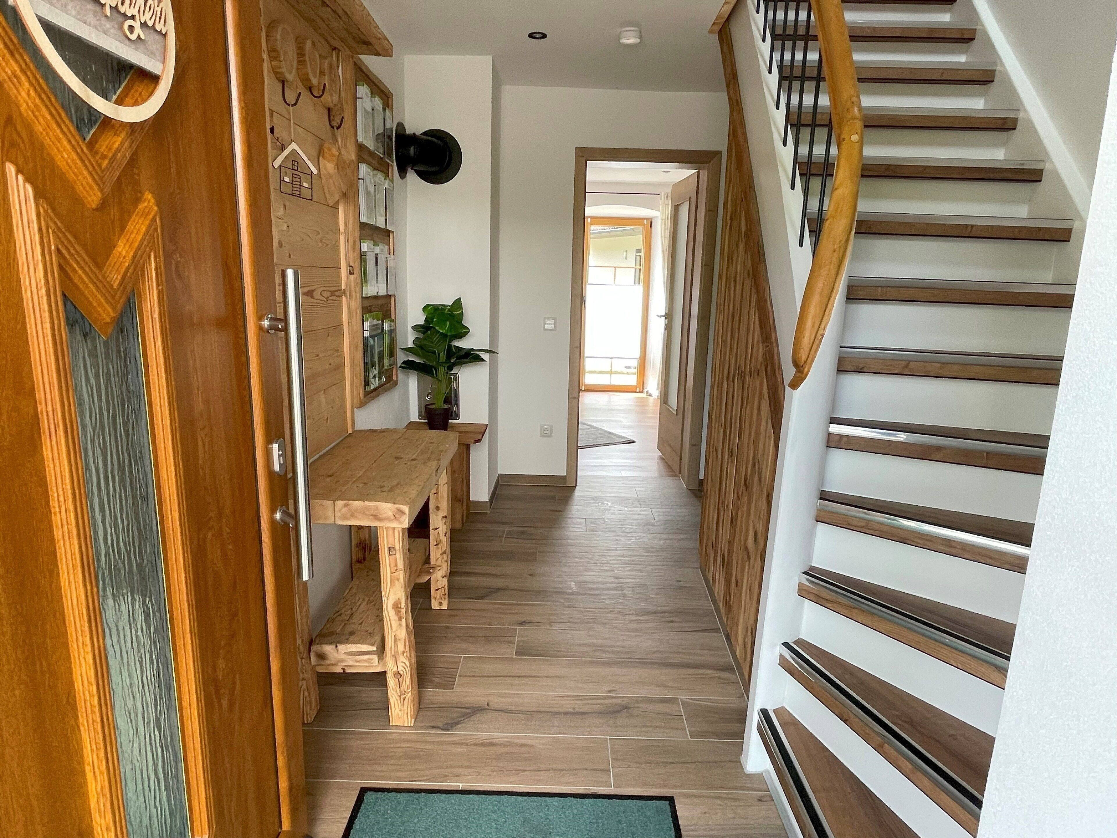 Un escalier en bois avec une rampe, un banc en bois et une porte ornée d’un motif décoratif.