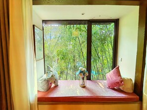 A room with a window seat, a vase with flowers, and a cushion.