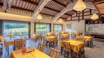 A restaurant with multiple tables and chairs, large windows, and a high ceiling with wooden beams.