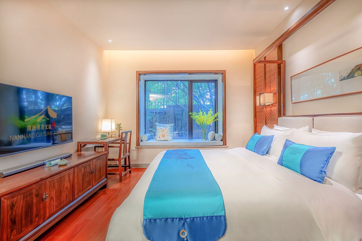 Une chambre d’hôtel avec un grand lit, une télévision, un bureau et une fenêtre donnant sur les arbres.