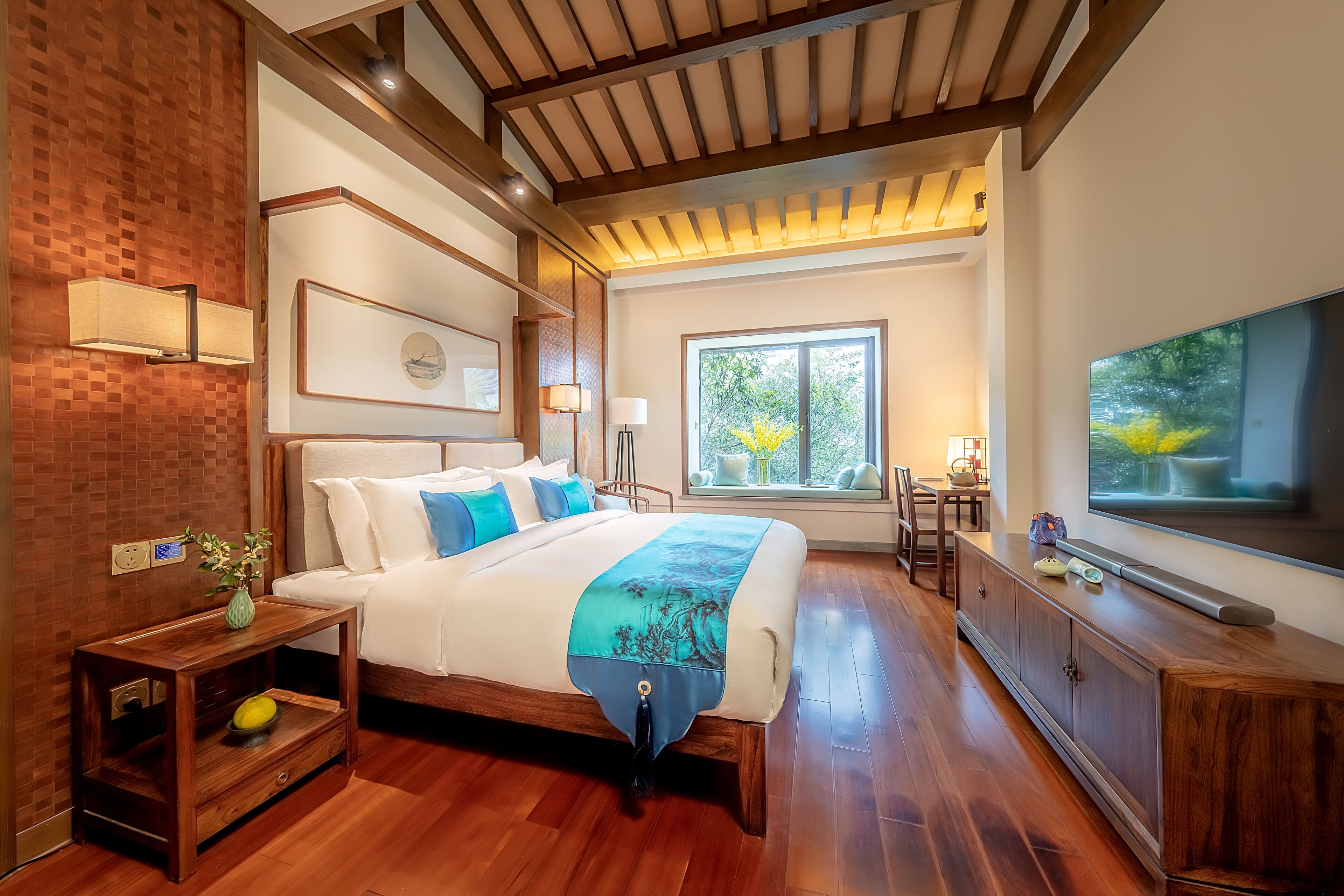 A modern bedroom with a large bed, a TV, and a window with a view of trees.