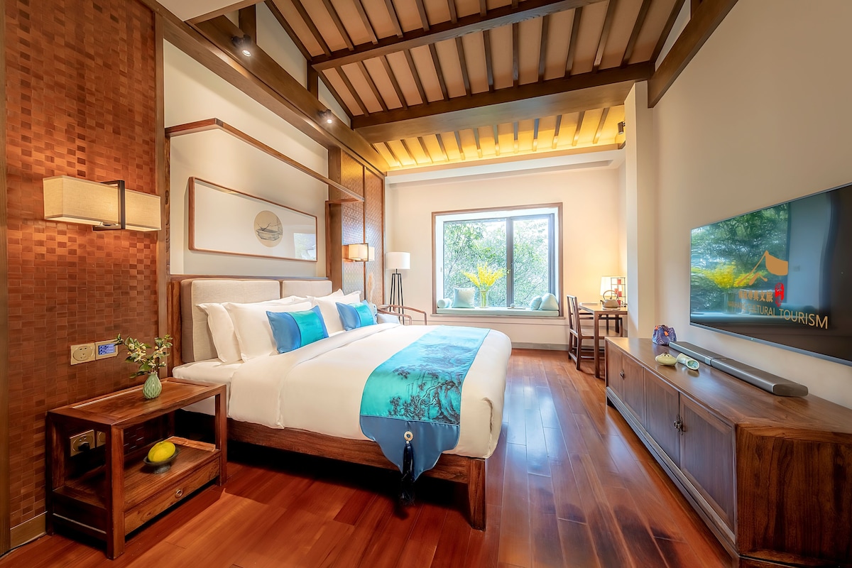 Une chambre moderne avec un grand lit, un plancher en bois, une télévision et une fenêtre donnant sur un paysage verdoyant.