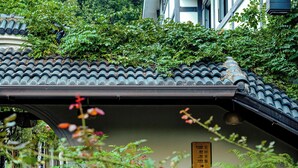 A traditional tiled roof with overgrown vegetation, a sign indicating a public toilet, and a partially visible building structure.