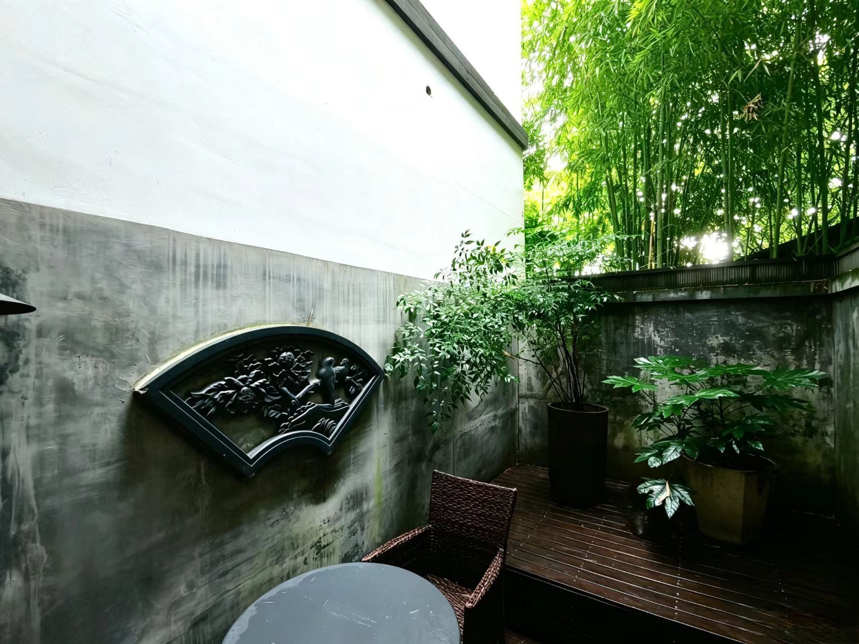 A courtyard with a concrete wall, a metal relief sculpture, a wicker chair, and potted plants.
