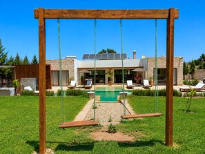 Ein Holzschaukelstuhl in einem Garten mit Swimmingpool und einem Haus im Hintergrund.