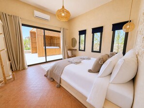 A bedroom with a large bed, a sliding glass door to a balcony, and a hanging light fixture. - Palais Kalya (Essaouira)