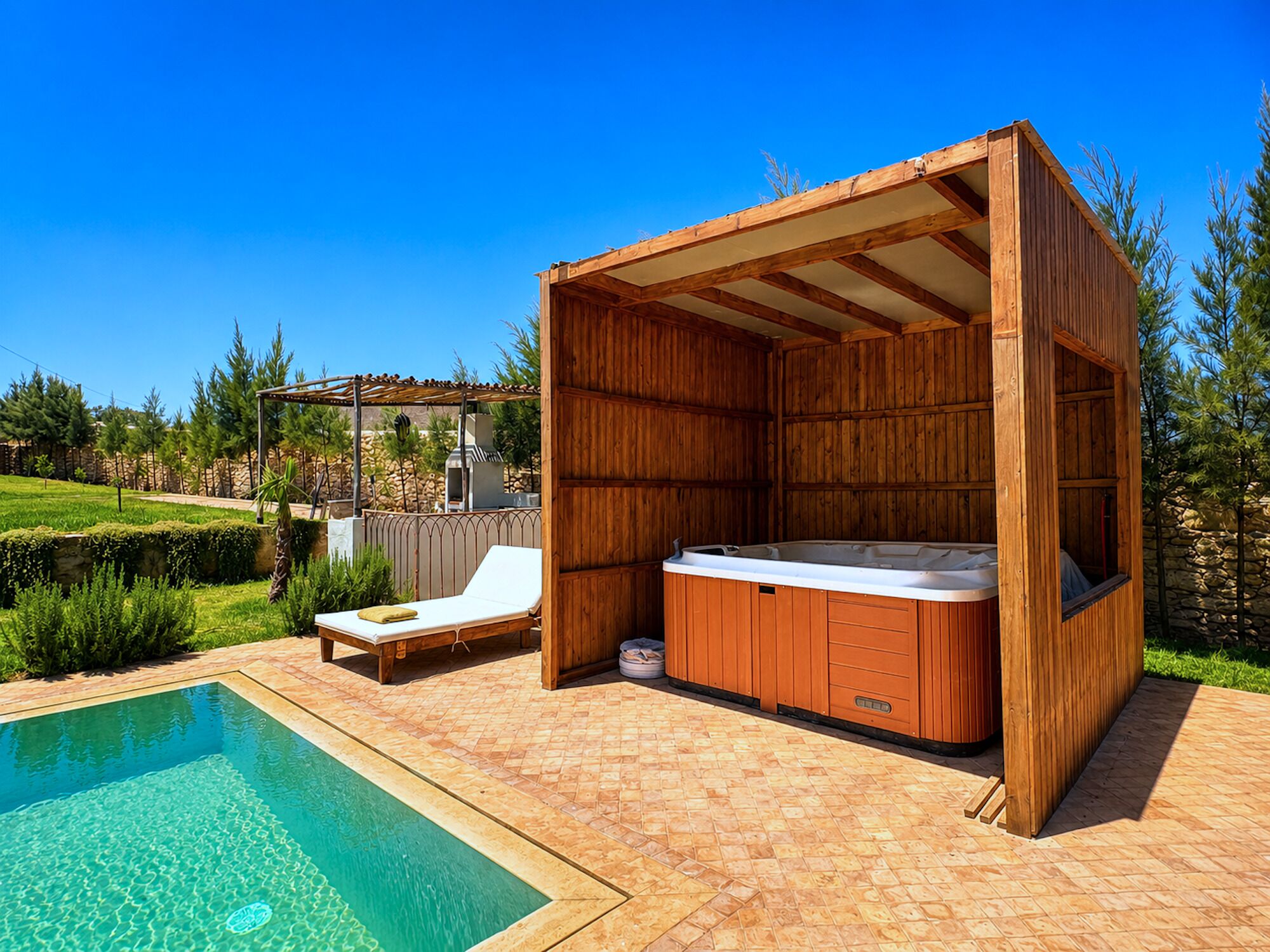 A wooden hot tub with a built-in seat, a lounge chair, and a pergola structure.