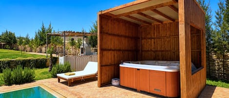 A wooden hot tub with a built-in seat, a lounge chair, and a pergola structure.