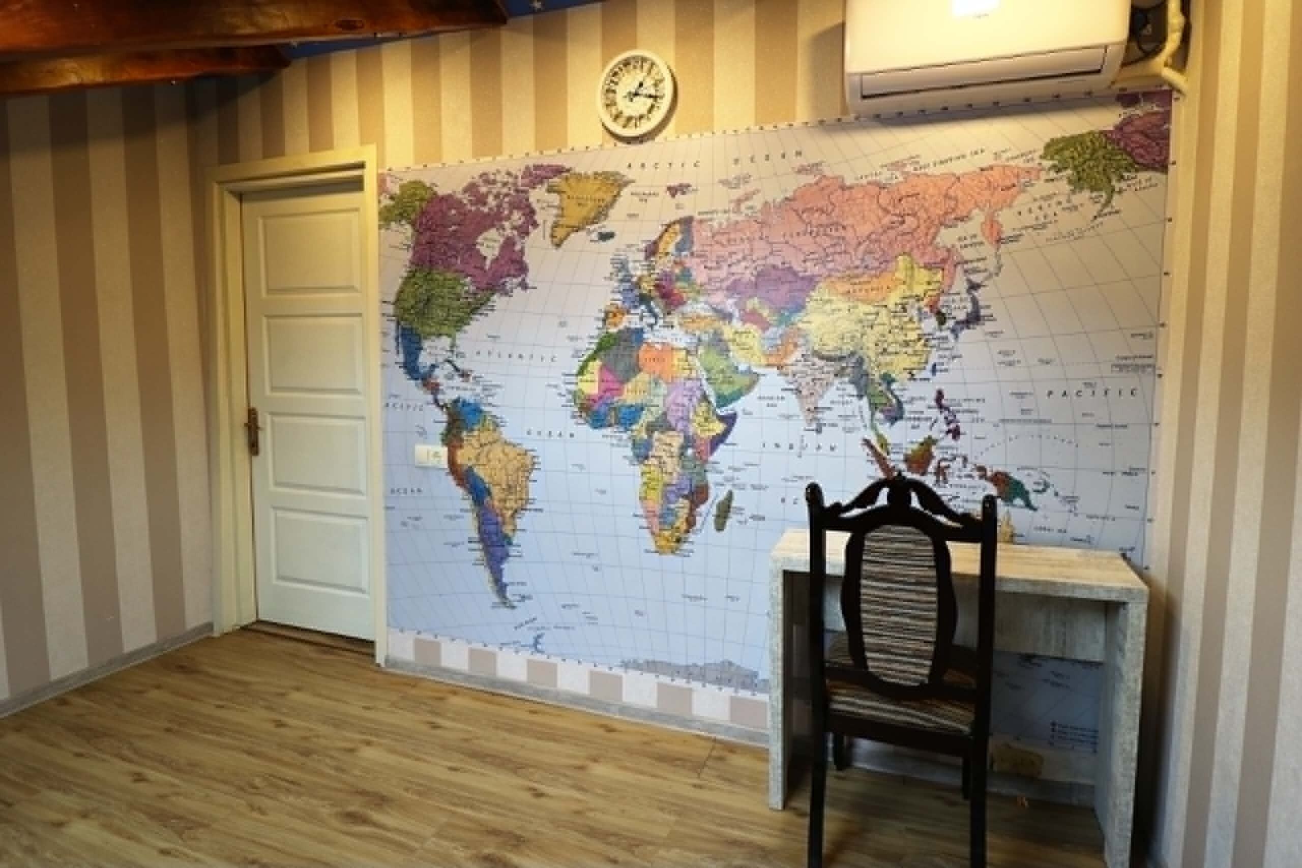 A room with a large world map on the wall, a wooden door, a chair, and a clock.