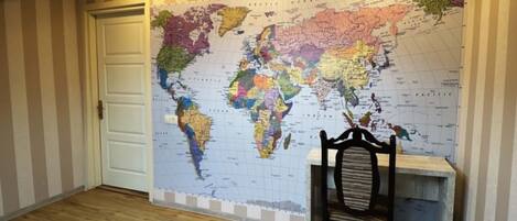 A room with a large world map on the wall, a wooden door, a chair, and a clock.