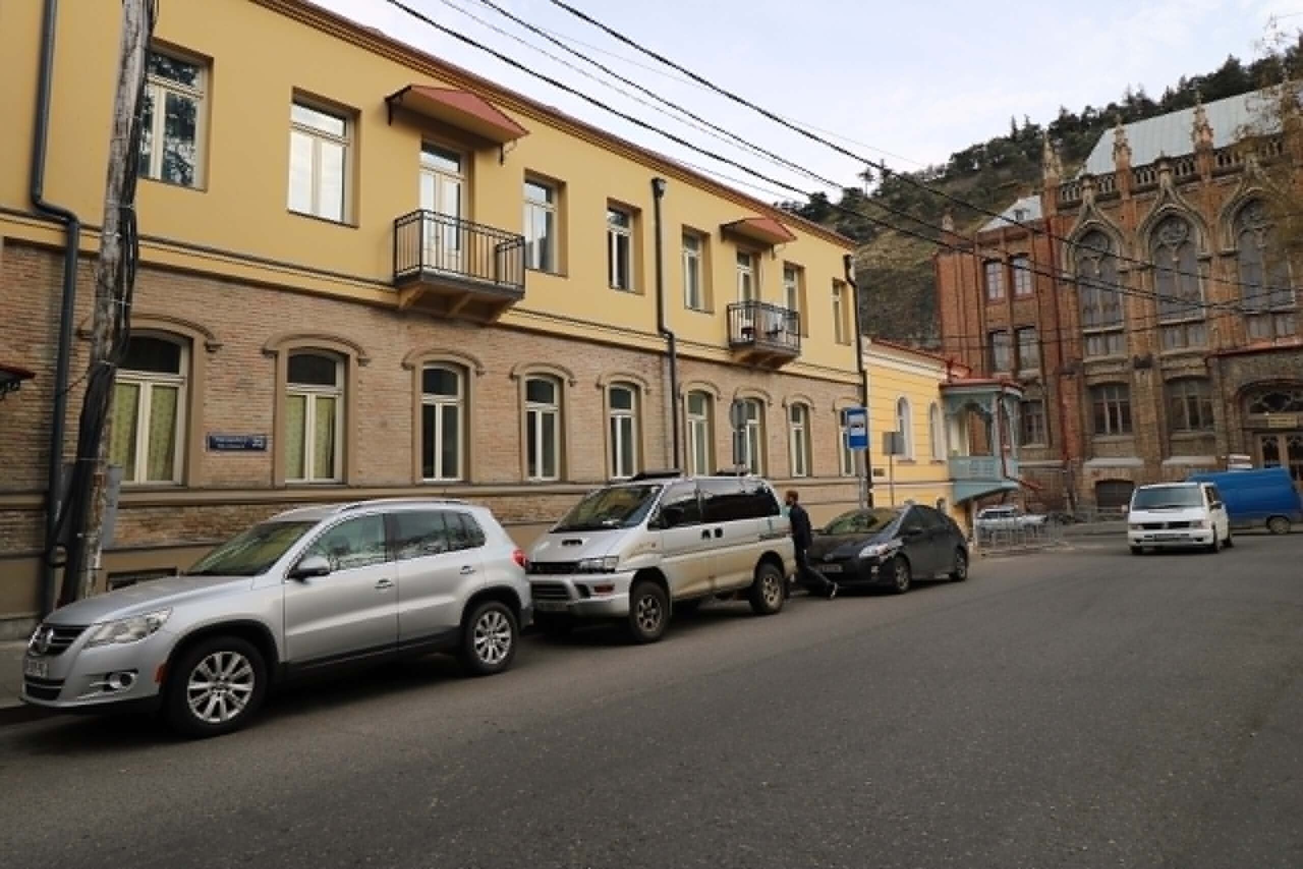 A street with parked cars and a building with a yellow facade and multiple windows.