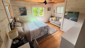 Una camera con un letto, un divano, una TV e una ventola a soffitto.