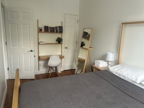 Un dormitorio con cama, escritorio, silla, estantería y espejo.