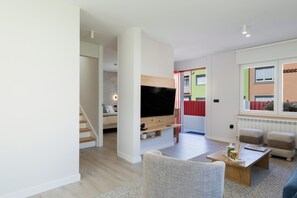 A modern living room with a flat-screen TV, a sofa, a coffee table, and a staircase leading to another room. - Grandma’s House – Renovated Seaside Home in Central Muxía with Garden & Parking (Muxía)