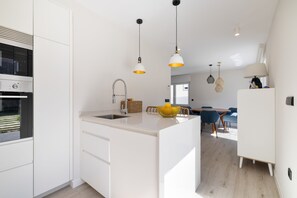 Eine moderne Küche mit Kochinsel, ein Essbereich mit rundem Tisch und ein Wohnbereich mit Sofa und Lampe.