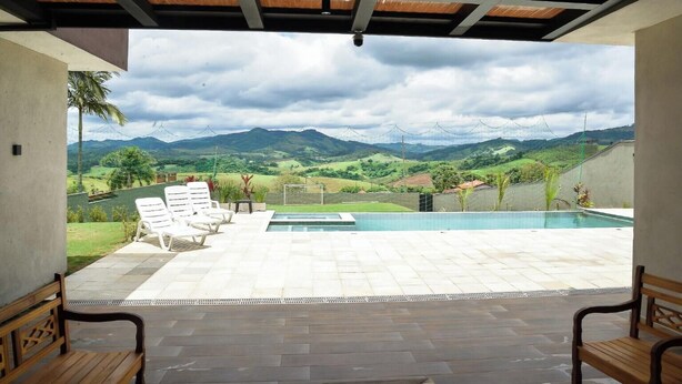 Un espace piscine avec vue sur les montagnes, un patio couvert et des sièges d’extérieur.