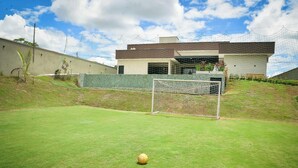 Un terrain de football avec des buts et un ballon, entouré d’une clôture et avec un bâtiment en arrière-plan.