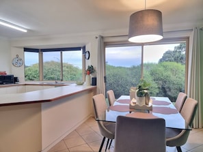 A modern kitchen with a dining area, large windows, and a view of greenery.