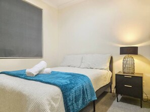 A bedroom with a bed, a nightstand, a lamp, and a wall-mounted artwork.