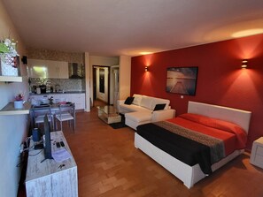 Ein kompakter Wohnbereich mit Küchenzeile, Essbereich und Schlafzimmer mit Bett und weißem Schlafsofa.