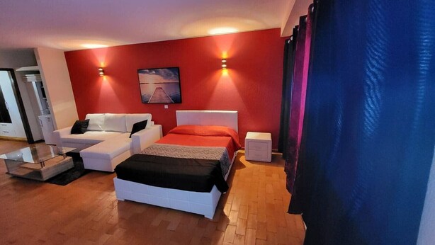 Une chambre à coucher comprenant un lit, un canapé, une table de chevet et un téléviseur fixé au mur.
