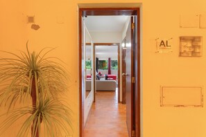 Ein Flur mit einem Blumentopf, einer Tür zu einem Zimmer mit Bett und Fenster sowie einer Wand mit einem Schild.
