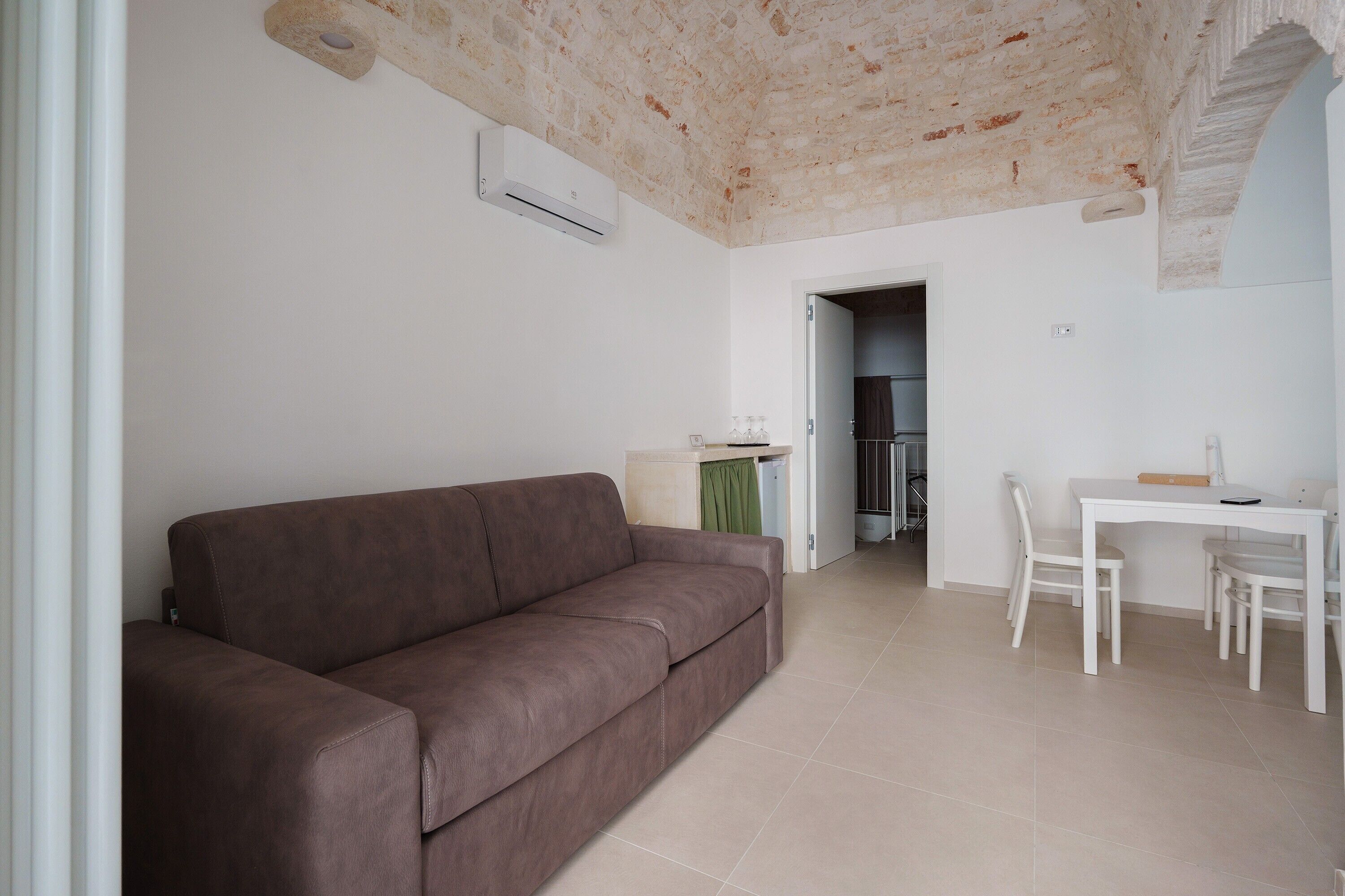 Ein Wohnzimmer mit braunem Sofa, einem weißen Esstisch mit Stühlen und einer Küche im Hintergrund.