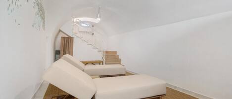 A minimalist room with a single white sofa, a wooden staircase, and a hanging light fixture.