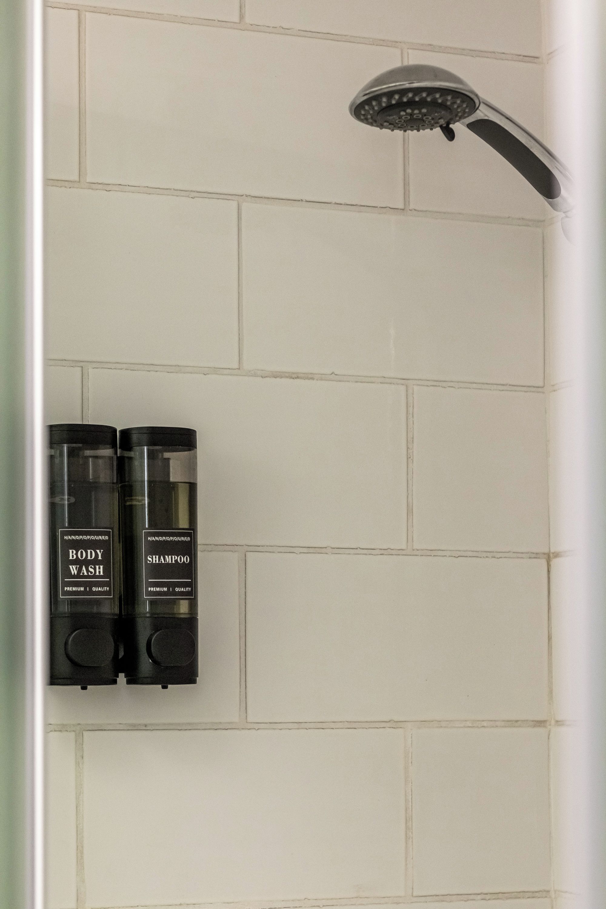 Zona doccia con soffione a pioggia e due flaconi di bagnoschiuma e shampoo.