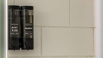 A shower area with a rain showerhead and two bottles of body wash and shampoo.