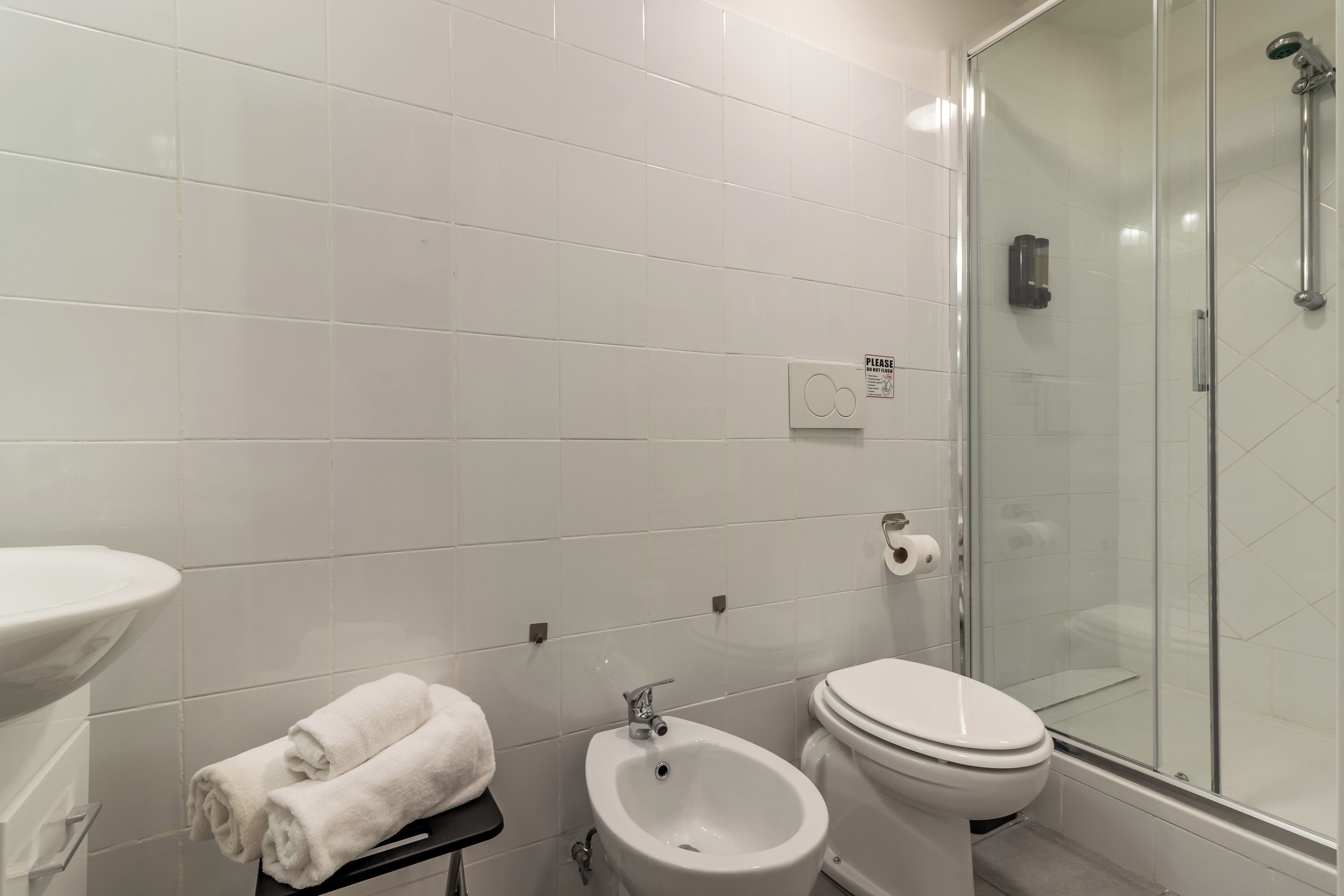 Un baño moderno con inodoro, bidé, lavamanos y cabina de ducha con mampara de vidrio.