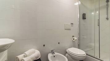 Un baño moderno con inodoro, bidé, lavamanos y cabina de ducha con mampara de vidrio.