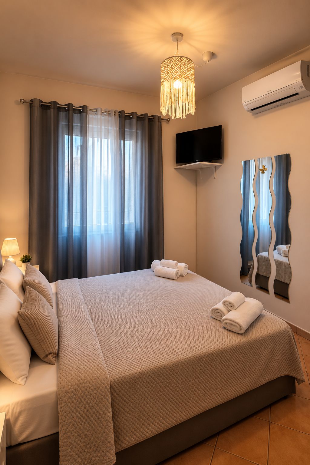A hotel room with a bed, curtains, a television, and a wall-mounted air conditioner.