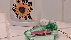Une salle de bain aux carreaux blancs, un distributeur de savon blanc orné de motifs de tournesols, et un objet décoratif vert parsemé d’étoiles dorées.