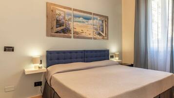 Un dormitorio con una cama grande, dos mesitas de noche con lámparas y una obra de arte colgada en la pared que representa una escena de playa.