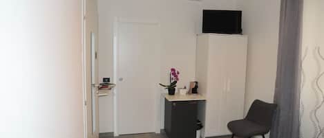 Habitación de hotel con cama, una silla, un escritorio con planta en maceta, televisor en mueble y equipo de aire acondicionado en la pared.