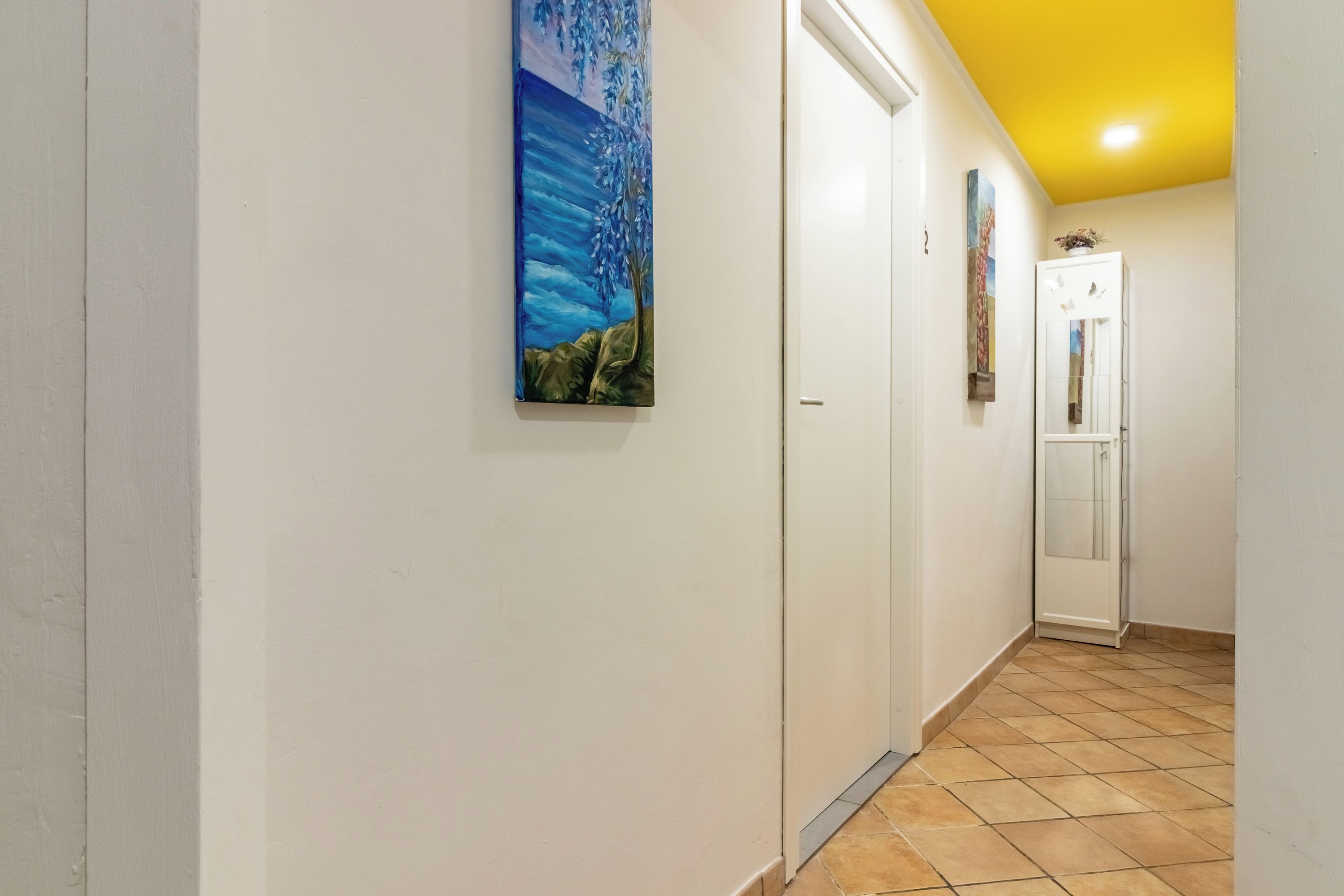 A hallway with white walls, a tiled floor, and a ceiling painted yellow.