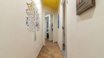 Un pasillo con un cuadro decorativo, suelo de baldosas y una puerta que da a otra habitación.