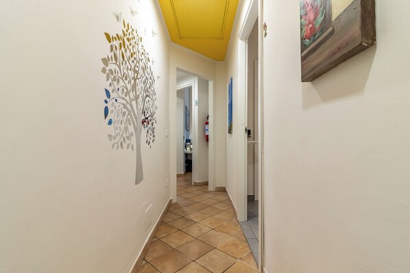 A hallway with a decorative wall art, a tiled floor, and a door leading to another room. - Cinqueterre in Fiore (La Spezia)
