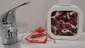 Un lavabo de salle de bain avec un robinet chromé, un distributeur de savon à motifs floraux et un objet décoratif orné d’un nœud.
