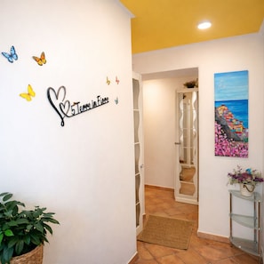 A hallway with a decorative sign, a potted plant, a glass door leading to a bathroom, and a painting on the wall.