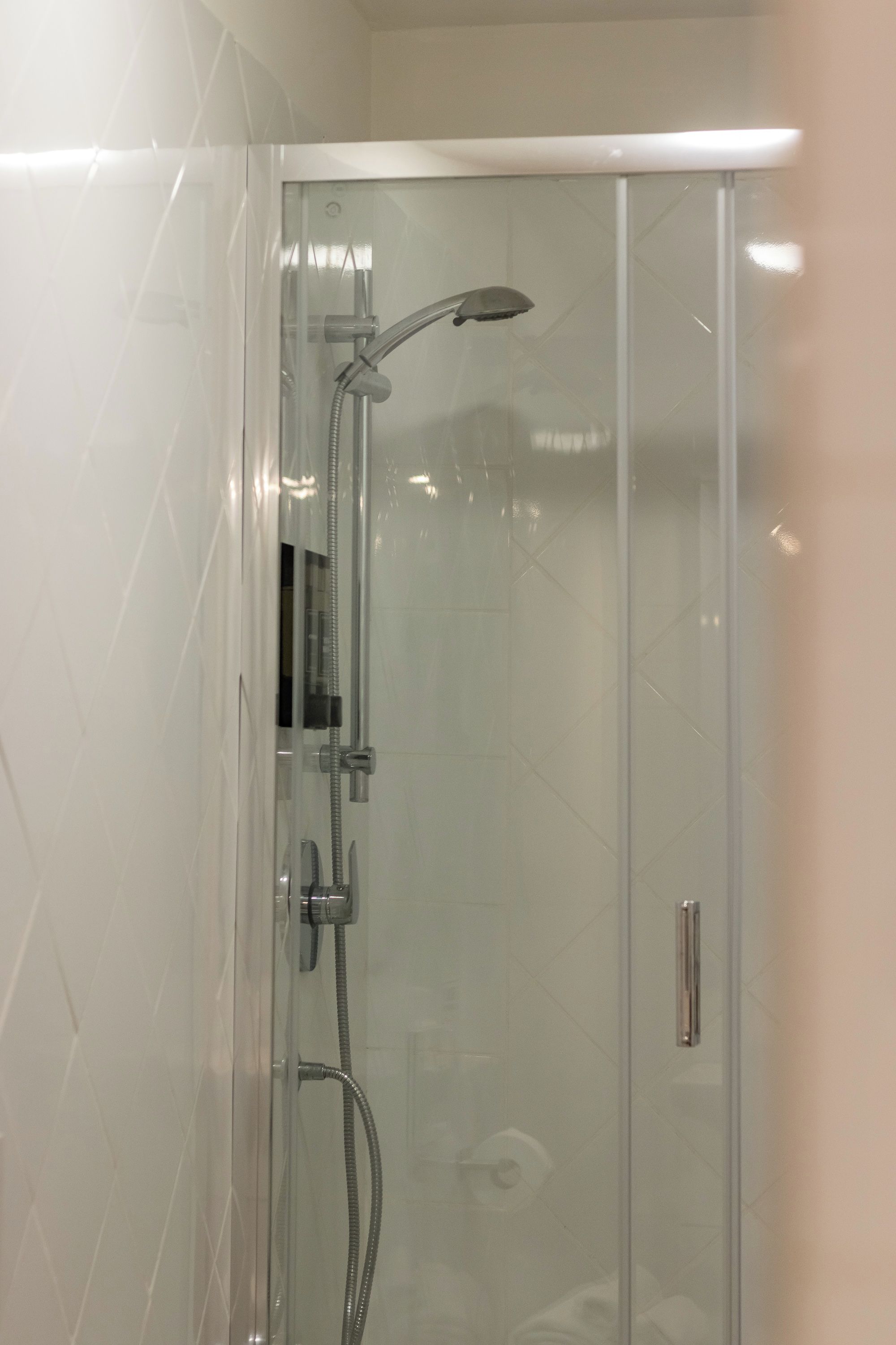 Cabina doccia in vetro con soffione a mano e rubinetto a flessello.