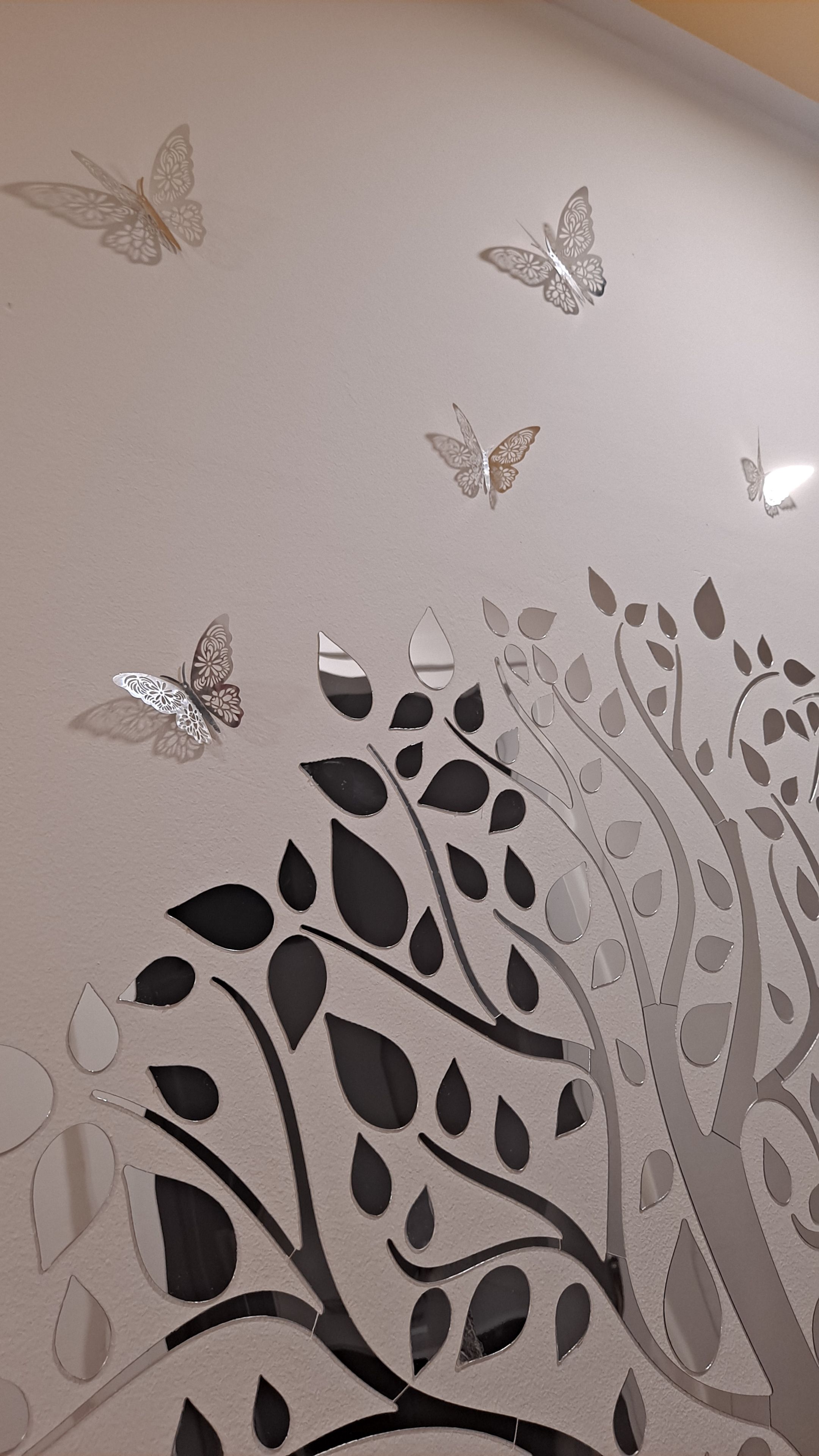 Un muro decorato con un disegno di un albero, foglie e farfalle.