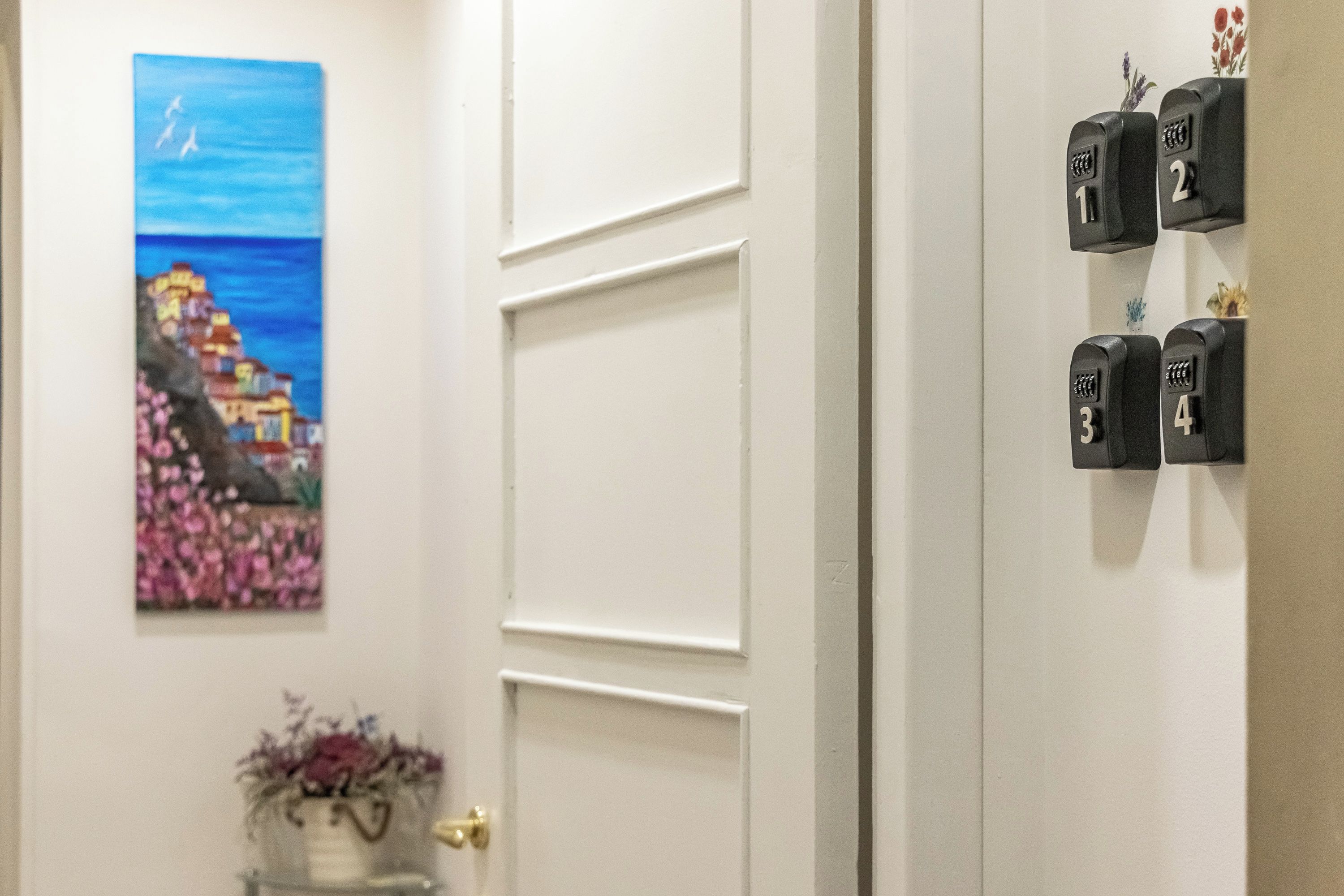 Un couloir avec une porte, un système de contrôle d’accès par badge fixé au mur et un tableau représentant un paysage côtier.