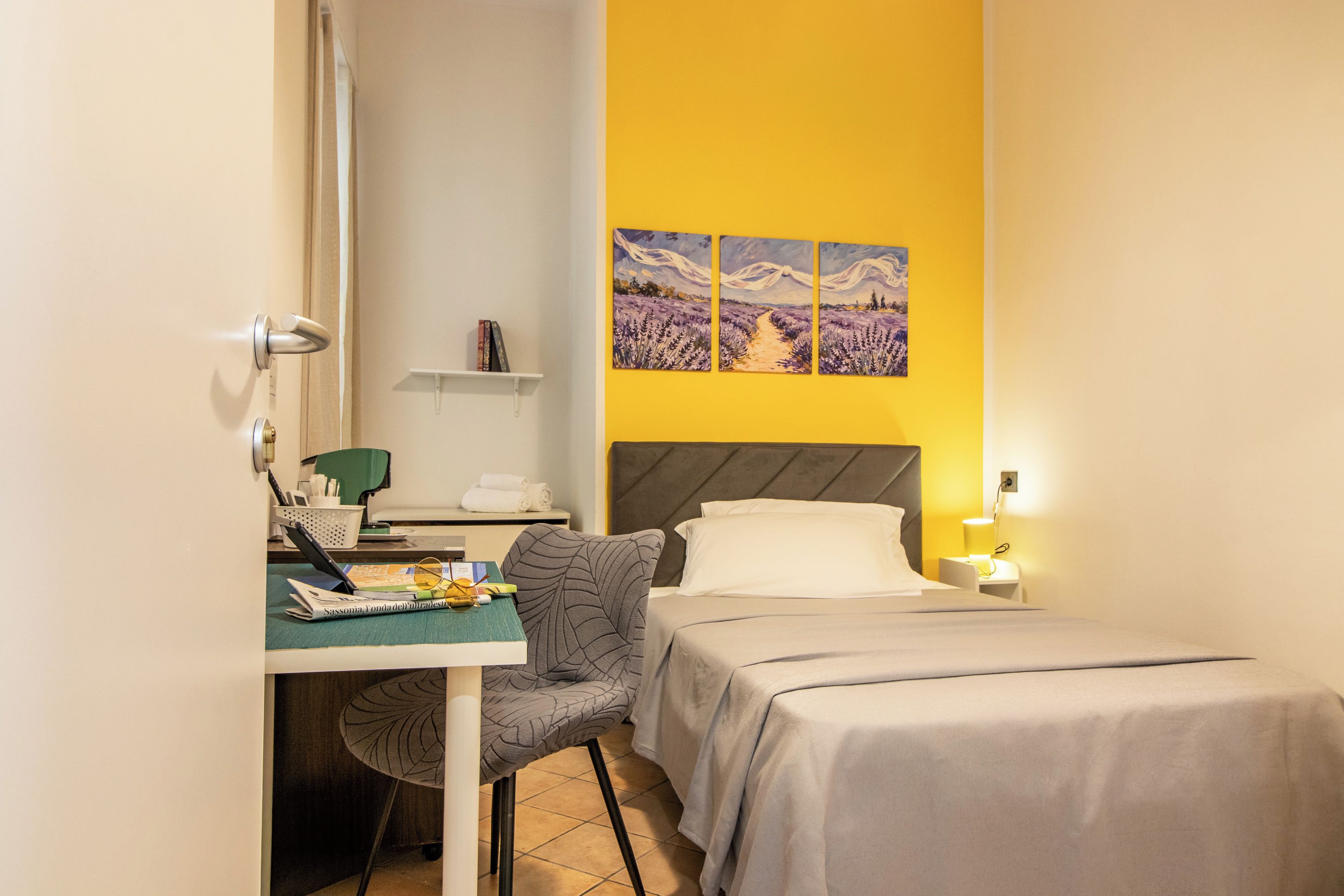 Une chambre d’hôtel comprenant un lit, un bureau avec une chaise, une petite table et un mur orné de trois tableaux.