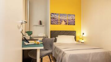 Une chambre d’hôtel comprenant un lit, un bureau avec une chaise, une petite table et un mur orné de trois tableaux.