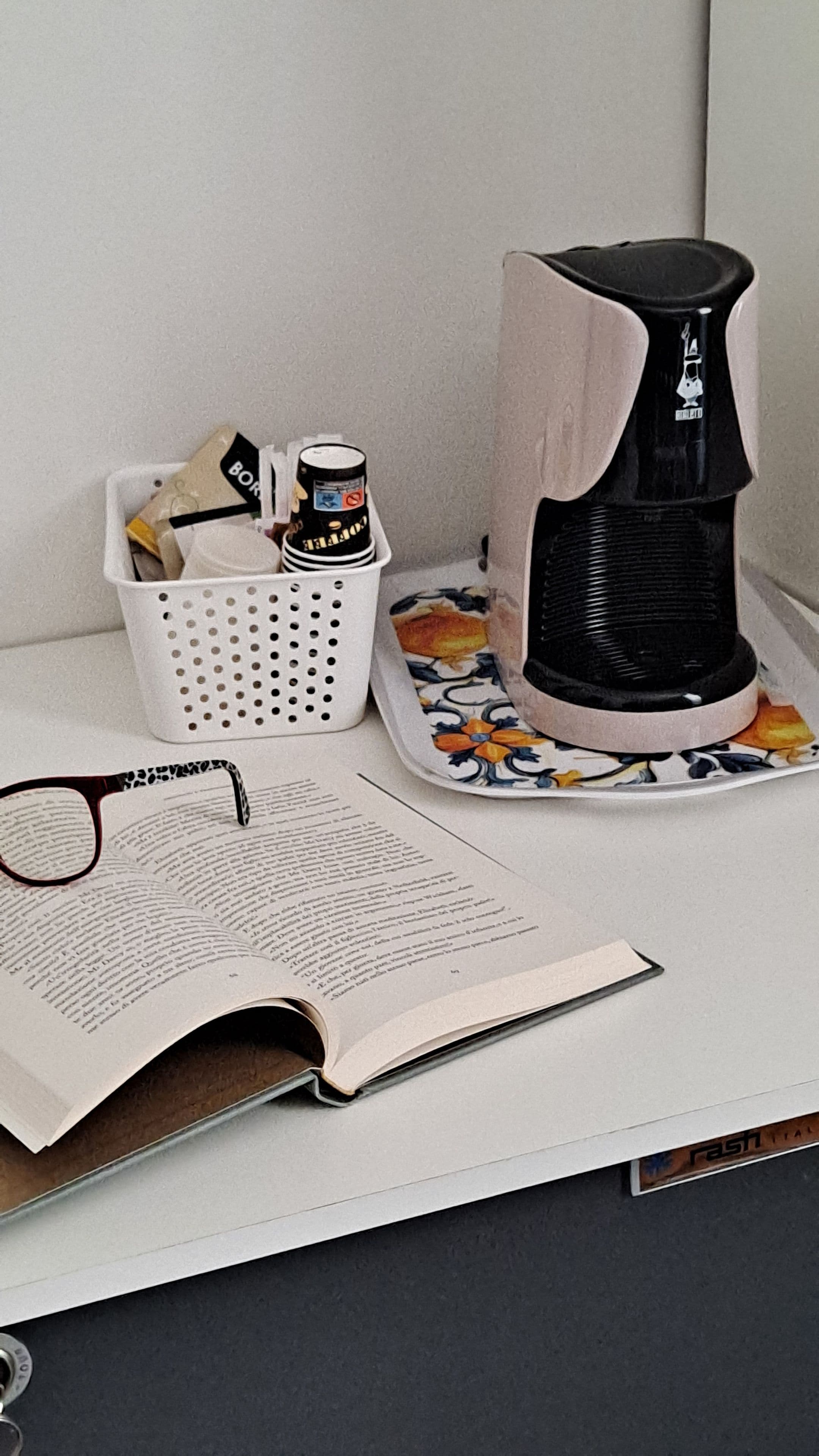 Une machine à café, un panier rempli d’objets et un livre ouvert sur une table.