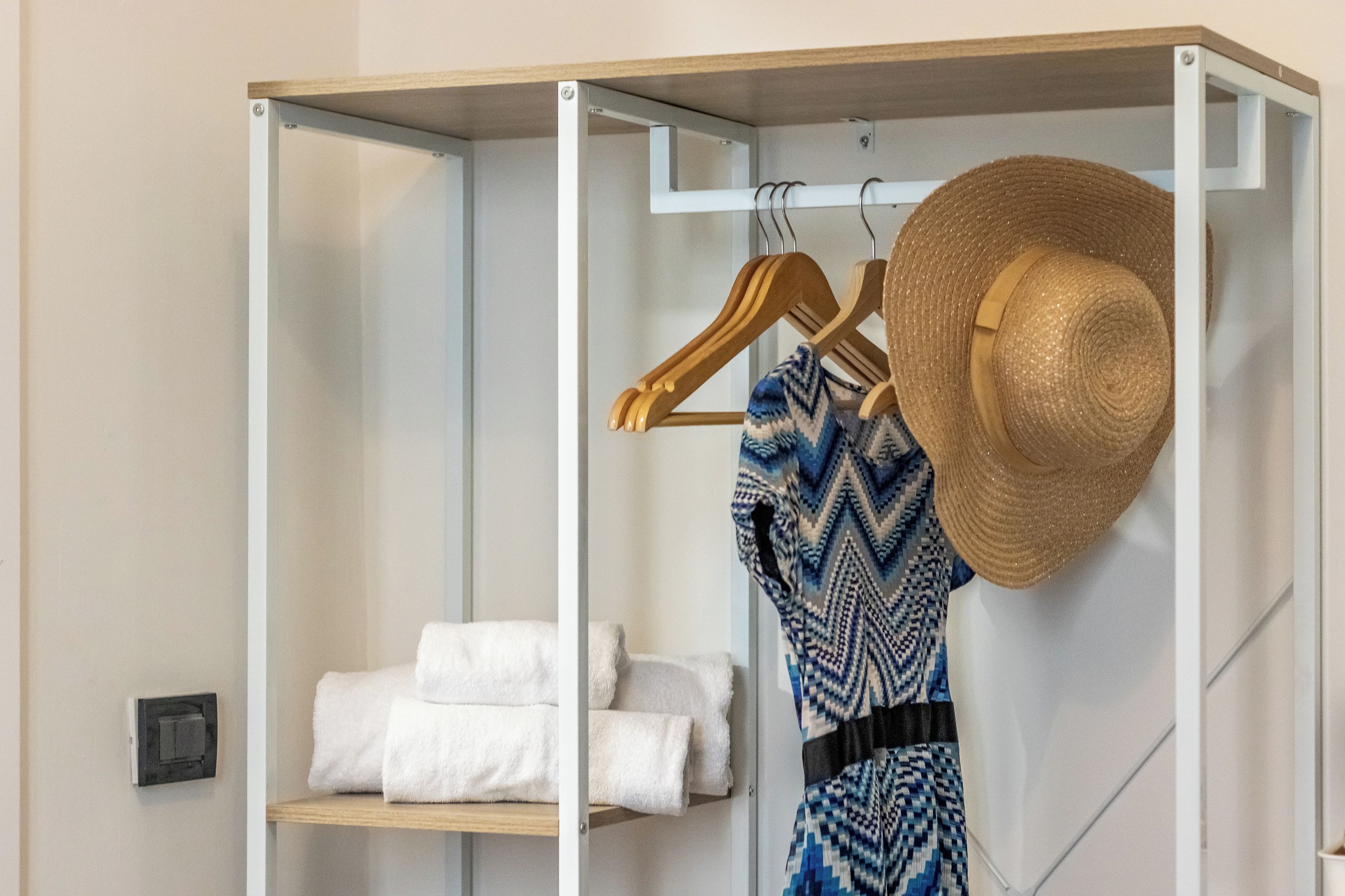A closet with hanging clothes and a hat, and a shelf with folded towels.