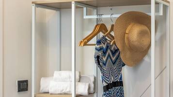 A closet with hanging clothes and a hat, and a shelf with folded towels.