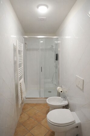 A bathroom with a glass-enclosed shower, a toilet, and a sink.